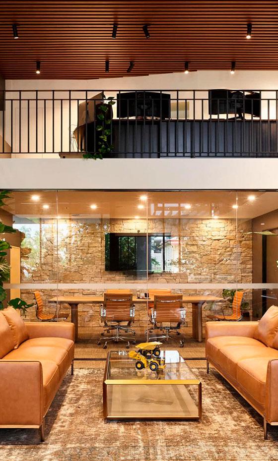 Architect-designed interior fitout at Railway Office Milton featuring a double-height workspace with timber ceiling battens, black steel detailing, glass meeting rooms, natural stone walls, warm leather seating and modern office furnishings.