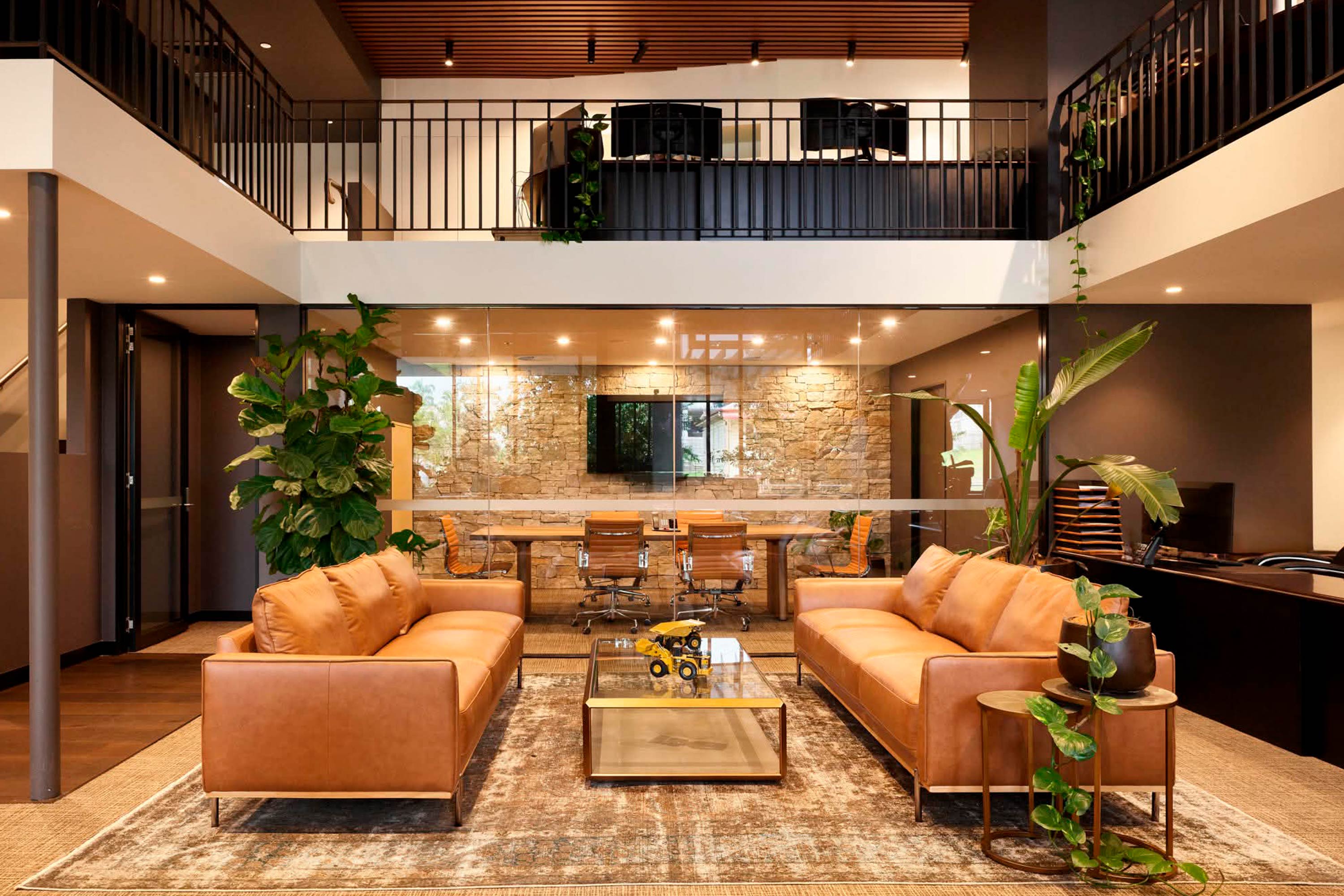 Architect-designed interior fitout at Railway Office Milton featuring a double-height workspace with timber ceiling battens, black steel detailing, glass meeting rooms, natural stone walls, warm leather seating and modern office furnishings.